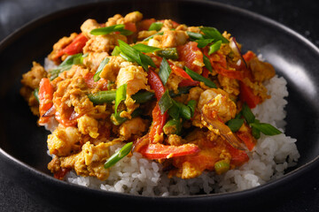 Thai breakfast Gai Pad Pongali with chicken, eggs, spicy, yellow thai curry paste,tomato, rice in black bowl made in wok. Close up. Pan-Asian cuisine. Close up.