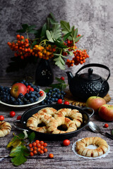 Fototapeta na wymiar Vertical autumn still life. Delicious apple rings in dough, rowan branches, grapes and apples on a dark wooden background