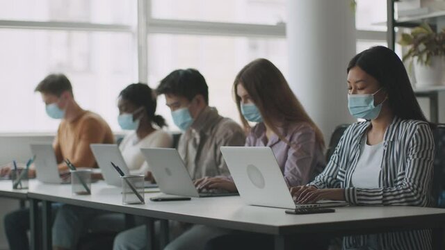 New normal and offline study concept. Group of diverse college students wearing protective face masks typing on laptops