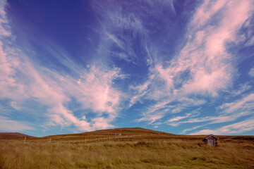 Old wooden hut on the hill against sunset cloudy sky on mountain