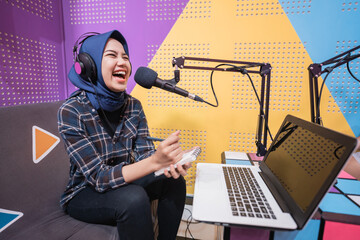 excited muslim woman is recording a podcast in studio with laptop