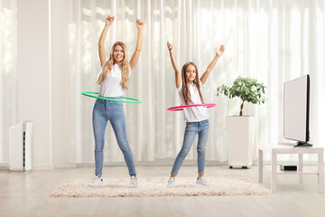 Happy mother and daughter spinning hula hoops at home