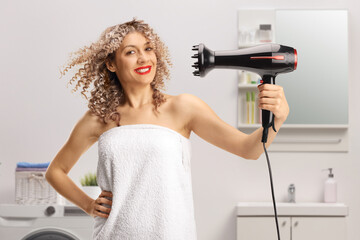 Woman with a curly hair wrapped in a towel using a hair diffuser in a bathroom