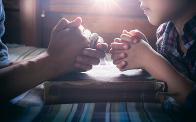 Close up hands of father and daughter praying on the Bible, focus hands.