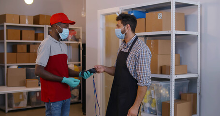 Small business owner in safety mask receive parcel and pay with credit card