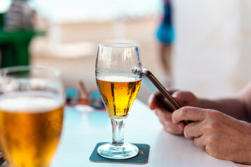 hands holding a mobile phone next to a glass of beer on the terrace bar