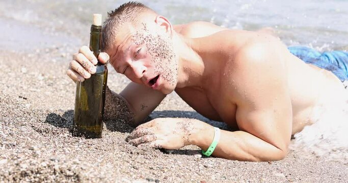 young drunk man on seashore lies with bottle of wine 4k movie