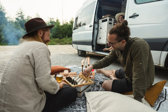 Male friends playing chess while spending leisure time by motor home