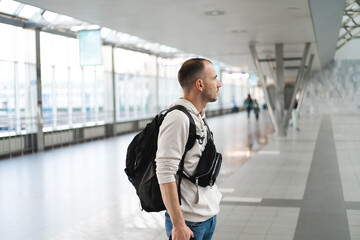 Young man with backpack stands in the airport or at the train station. Copy space.