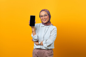 Cheerful Asian woman showing smartphone blank screen over yellow background