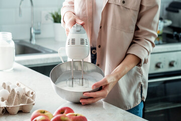 A woman in the kitchen whips chicken whites with sugar with a mixer to make an apple pie. Cooking.