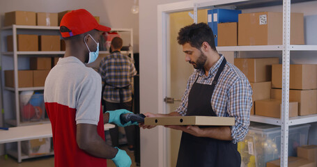 Courier in mask deliver pizza to warehouse workers