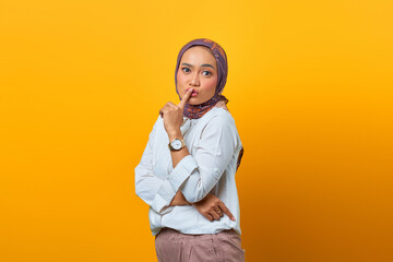 Beautiful Asian woman making finger on lips mouth silent quiet gesture over yellow background