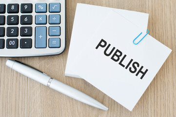 The text PUBLISH on a white card on the table next to a calculator and a pen
