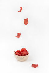 Raw smoked pork chips with spices in a ceramic bowl on a white textured background. A few pieces fall from above into the bowl. Appetizer for beer. Levitation, vertical orientation.