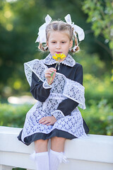 Happy little schoolgirl in uniform holding flower. Summer in the park.