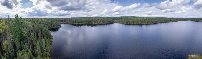 Aerial of a wilderness lake in the forest with reflection of trees and clouds in the water.
