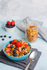 A blue bowl of refreshing mixed berries cereal and a metal spoon, with a jar of cereal and a small bowl of mixed berries