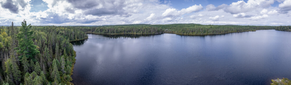 Aerial of a wilderness lake in the forest with reflection of trees and clouds in the water.
