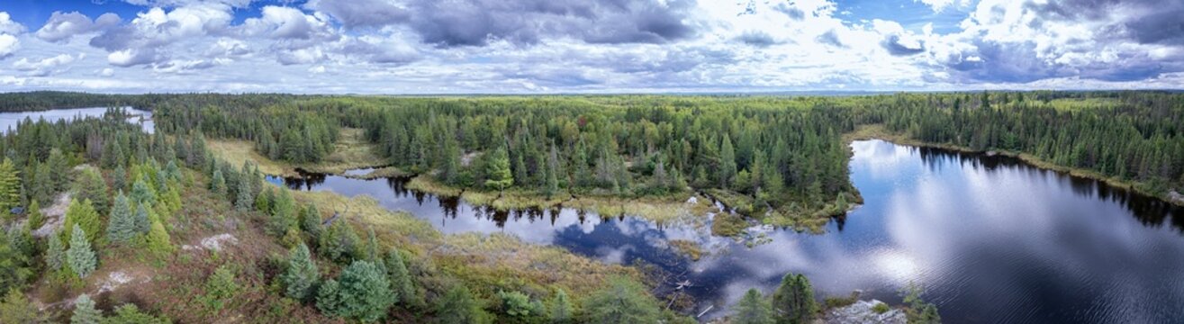 Aerial of a wilderness lake in the forest with reflection of trees and clouds in the water.