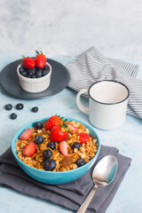 A bowl of mixed berries cereal with a white coffee cup and a bowl of berries at the background