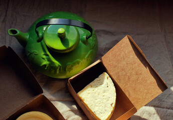 Homemade farm piece of cheese in box and green teapot on the table 