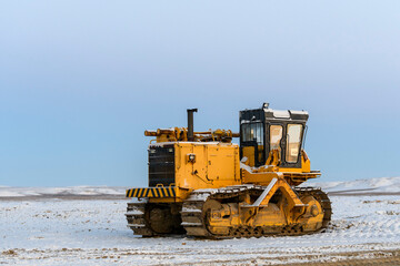 Yellow tractor in winter tundra. The road construction.