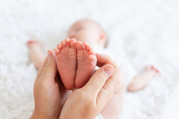 the legs of a newborn baby in my mother's hands on a white background of the bed close-up , my mother's love and care