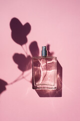 Transparent bottle of perfume on a pink background. Fragrance presentation with daylight. Trending...