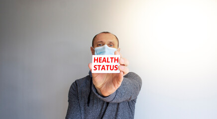 Health status symbol. White card, words Health status. A young man in a grey wear and medical mask. Sunshine. Beautiful white background. Medical, health status concept.