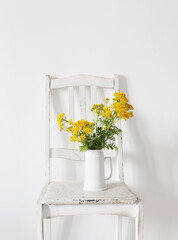 bouquet of tansy on  old wooden chair in  white interior