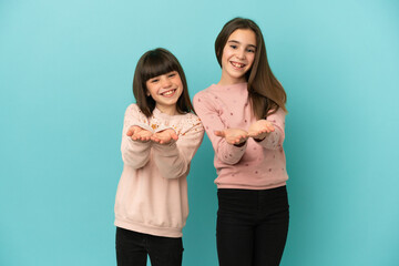 Little sisters girls isolated on blue background holding copyspace imaginary on the palm to insert...