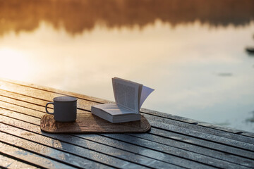 cup of coffee and book on wooden pier on summer lake