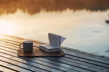 Zelfklevend Fotobehang cup of coffee and book on wooden pier on summer lake © Maya Kruchancova