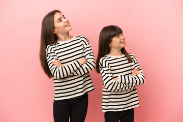 Little sisters girls isolated on pink background looking up while smiling