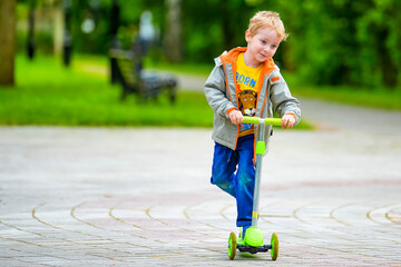 Little five-year-old child, smiling boy rides an electric scooter in a summer park. Active children's outdoor sports. Healthy lifestyle in childhood. © Евгений Панов