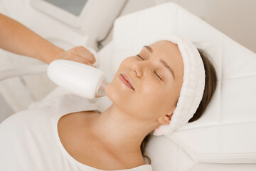 Young woman having laser hair removal procedure of face zone by specialist in cosmetic center....