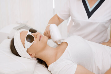 Young woman having laser hair removal procedure of face zone by specialist in cosmetic center....