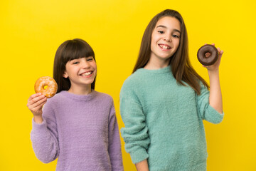 Little sisters isolated on yellow background holding a donut and happy