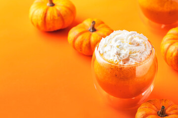 Orange pumpkin latte with whipped cream in glass cup. Autumn or winter hot drink in festive table setting