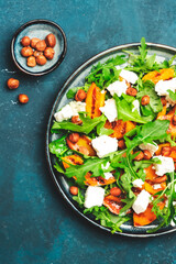 Grilled peach salad with feta cheese, hazelnuts and arugula on blue background, top view, copy space