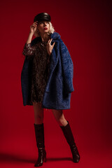 Fashionable blonde woman wearing trendy faux fur blue coat, cap, sequin mini dress, marsala color...