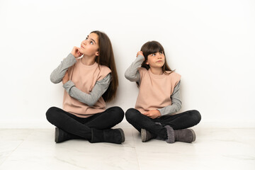 Little sisters sitting on the floor isolated on white background thinking an idea while scratching head