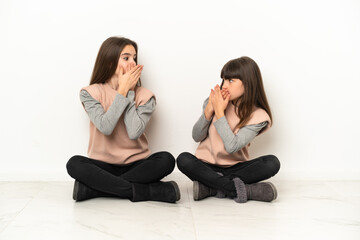 Little sisters sitting on the floor isolated on white background covering mouth with hands for...