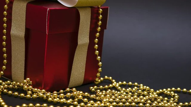 Beautiful red gift box with a gold bow and beads on a black background. A perfect gift for any occasion such as christmas or birthday.