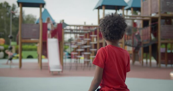 Back view of preschool african boy sit on bench on outdoors playground
