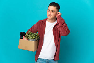 Young caucasian man making a move while picking up a box full of things isolated on blue background...