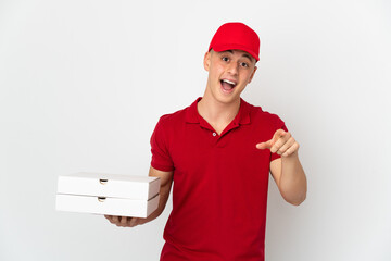 Pizza delivery man with work uniform picking up pizza boxes isolated on white background surprised and pointing front