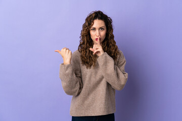 Young caucasian woman isolated on purple background pointing to the side and doing silence gesture