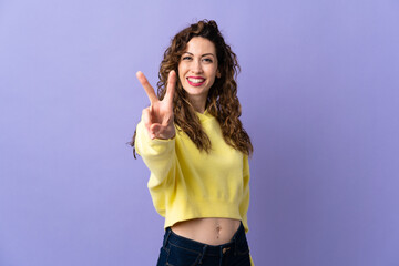 Young caucasian woman isolated on purple background smiling and showing victory sign